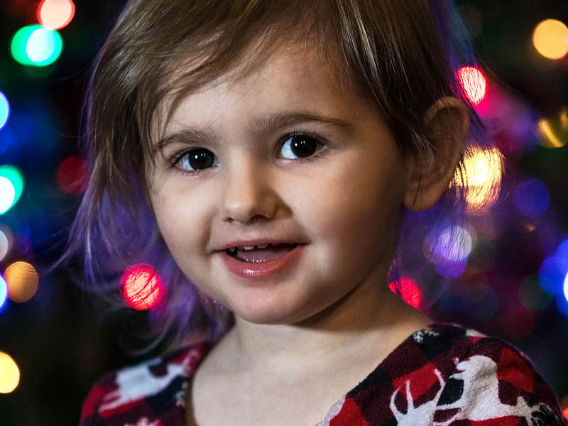 young girl smiling with christmas tree lights