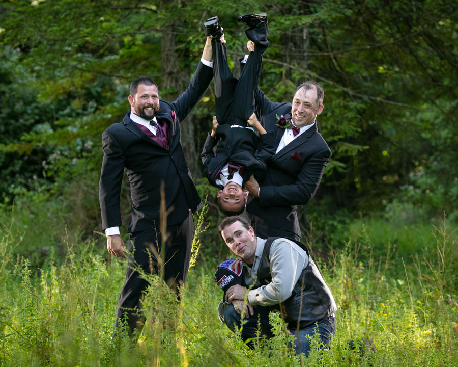 groom and best man holding boy upside down